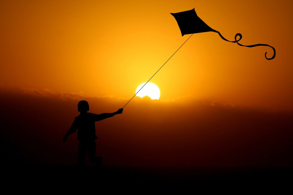 boy running with a flying dragon in sunset