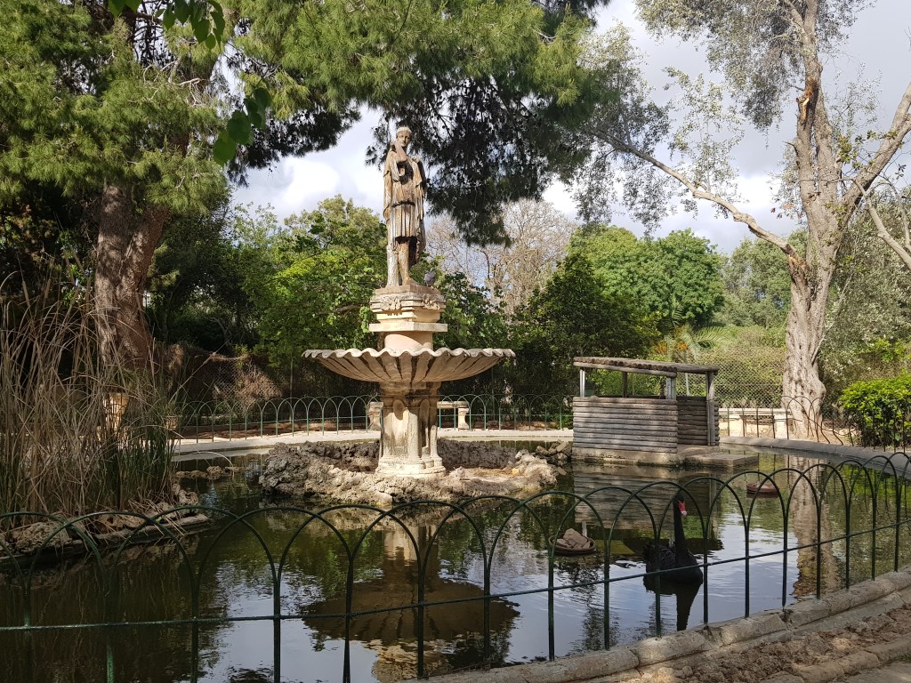a pond with a statue at its center and a black swan swimming in it