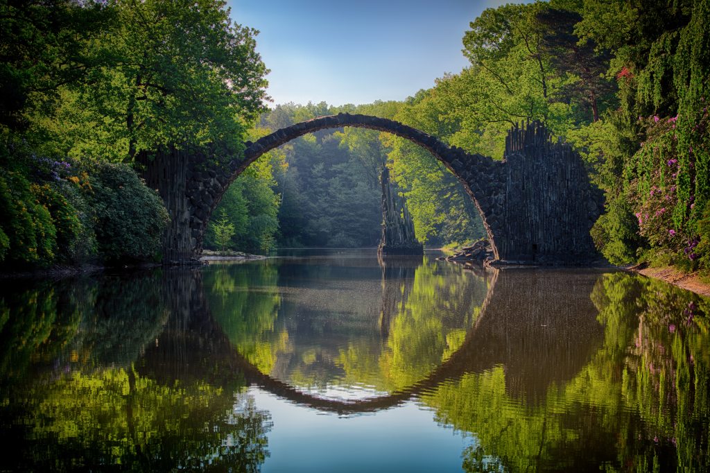 arch bridge of stone over a body of water with clear reflection in the water