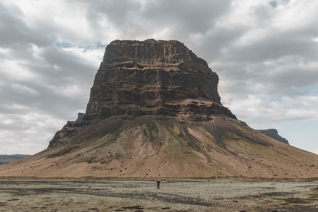 a photo of a large old cliff mountain in the middle of a flat landscape
